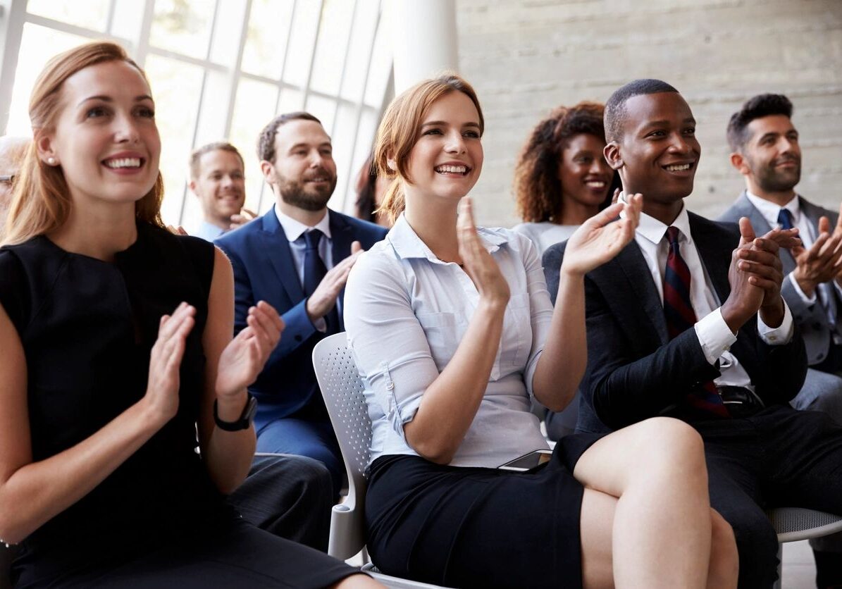 Diverse group of employees smiling and clapping at a presentation